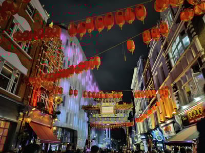 Red lanterns lighting up the lively Chinatown district at night, with a traditional arch in the background.