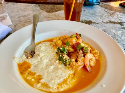 Shrimp with grits in spicy sauce, served at the Red Rooster bar, accompanied by a refreshing iced tea.