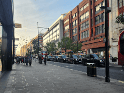 Rue Oxford animée, avec des piétons et des voitures, entourée de boutiques modernes sous un ciel clair.