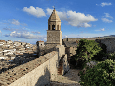 Tour médiéval du Château de Bovino avec son clocher et une vue panoramique sur les maisons environnantes sous un ciel bleu.