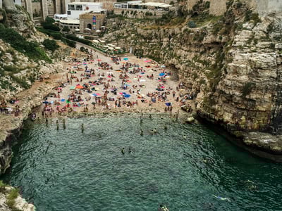 Plage animée à Grotta Piana, avec des baigneurs profitant de l'eau turquoise et du soleil sur le sable.