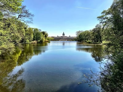 Peaceful reflection of Charlottenburg Palace in the pond, surrounded by lush trees under a clear blue sky.
