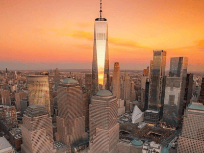 Aerial view of Midtown Manhattan at dusk, showcasing the One World Trade Center radiating light.