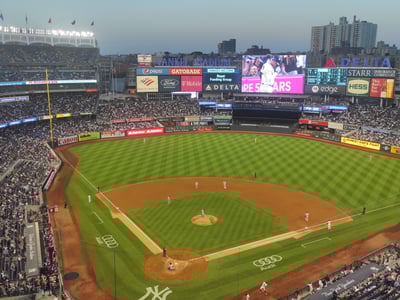 Stade Yankee rempli de fans, éclairé pour un match de baseball, avec un terrain bien entretenu et le grand écran en arrière-plan.