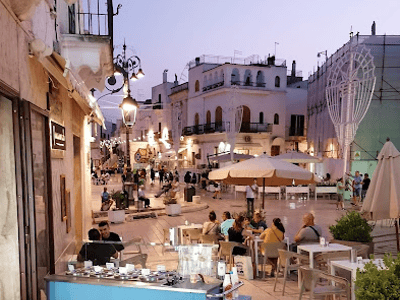 Terrasse animée d'Osteria Pugliese, avec des visiteurs profitant d'une soirée paisible dans une rue pittoresque.