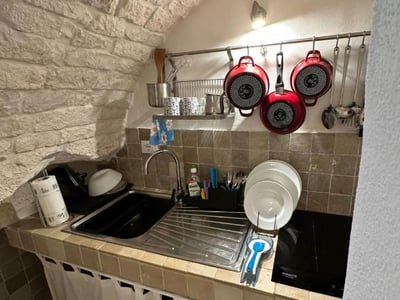 Modern kitchen with stone walls at La Chicca di Ostuni, including a sink, utensils, and cooking equipment.