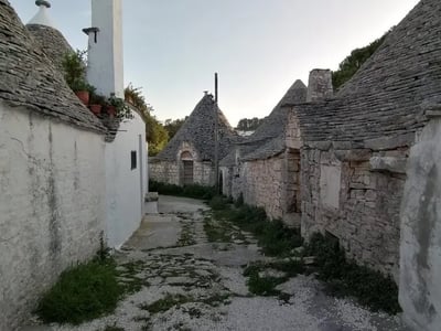 Ruelle tranquille du Quartier Aia Piccola, avec des trulli en pierre et une végétation luxuriante aux abords.