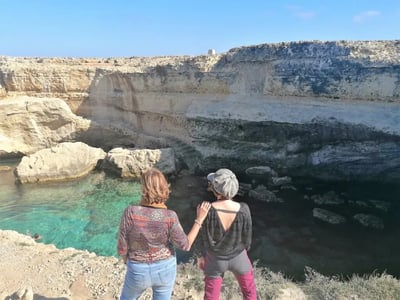 Two people admire the spectacular landscape of the Poetry Caves, with turquoise waters and majestic cliffs.