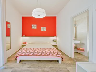 Chambre lumineuse au ILICE B&B, avec un mur rouge vibrant, lit douillet et salle de bain moderne adjacente.