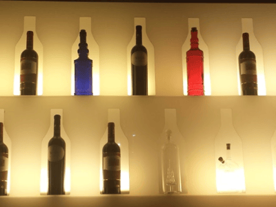 Des bouteilles de différentes couleurs illuminées, décorant le mur d'Il Quinto, offrant une ambiance unique et élégante.