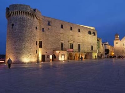Château historique de Conversano éclairé la nuit, mettant en valeur son architecture médiévale et son ambiance charmante.