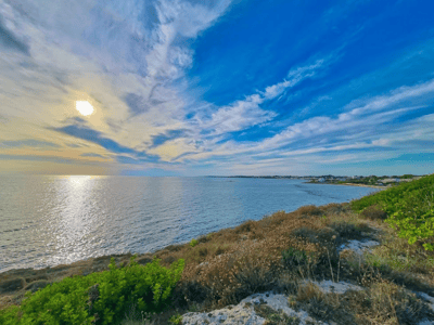 Panoramic view of Torre Ovo, with the sun reflecting on the water and lush green hills in the foreground.