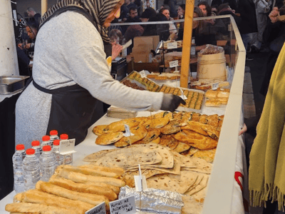 Saleswoman at Markhalle Neun presenting a variety of traditional pastries at a lively stall.