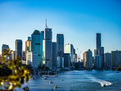 Vue panoramique de la skyline de Brisbane au bord de la rivière, avec des bateaux de plaisance et un ciel dégagé.