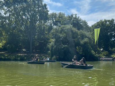 Families in boats are enjoying a sunny day at the lake, surrounded by lush nature.