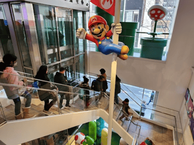 Mario brandissant un drapeau dans le magasin Nintendo, entouré de personnages et éléments emblématiques de l'univers des jeux vidéo.