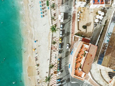 Plage de Jávea vue du ciel, avec des parasols, des baigneurs et la promenade bordée de palmiers.