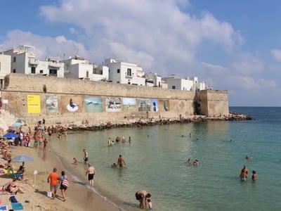 Plage animée à Monopoli, avec des baigneurs profitant des eaux claires devant des murs ornés de fresques.