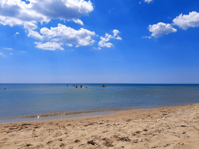 Plage de Castellaneta Marina, avec des vacanciers profitant du soleil et des eaux tranquilles sous un ciel bleu parsemé de nuages.