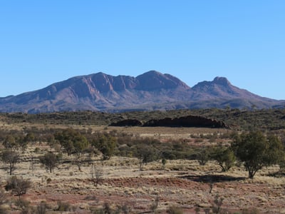Montagnes majestueuses des West MacDonnell Ranges, avec un ciel bleu clair et des paysages arides en premier plan.