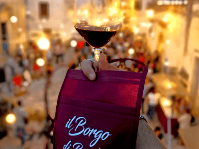 Un verre de vin rouge porté au-dessus d'une foule joyeuse lors de l'événement Cortili Aperti à il Borgo di Bacco.