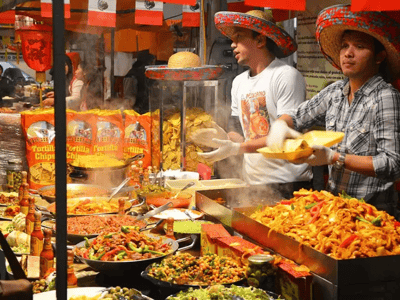 Smiling vendors preparing colorful dishes at the Upmarket Brick Lane Food Hall, attracting food lovers with their specialties.