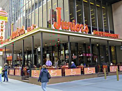 Junior's Restaurant in New York, with customers enjoying meals on the terrace under a catchy sign.