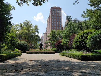 A well-maintained garden in Gramercy Park, surrounded by modern buildings and lush greenery under a sunny sky.