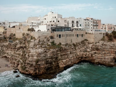 Côte rocheuse de Bari avec des bâtiments historiques surplombant la mer turquoise, reflétant le charme méditerranéen.