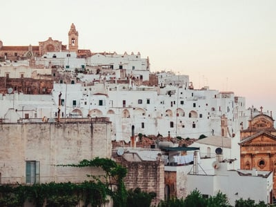The characteristic white houses of Ostuni, with old walls and the silhouette of a church at the top, at sunset.