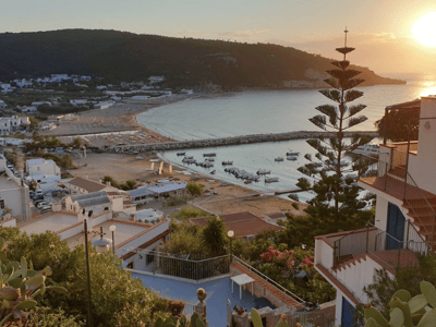 Panoramic view of the beach of Peschici at golden hour, with anchored boats and hills in the background.