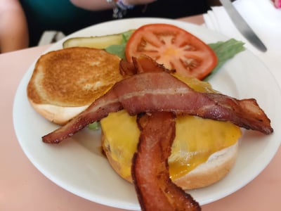 A tasty burger with melted cheese, crispy bacon, fresh tomatoes, and pickles, at Lexington Candy Shop.