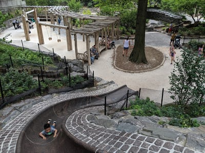 Slide of a child in the Billy Johnson Playground, with wooden play structures and families enjoying the green space.