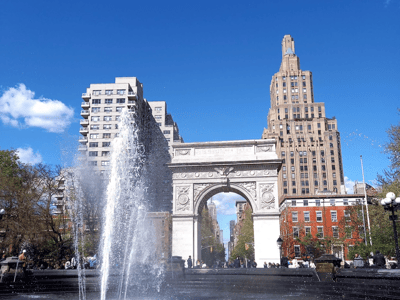 Fontaine jetant de l'eau avec l'Arc de triomphe à Washington Square, entouré de bâtiments emblématiques et d'un ciel bleu clair.