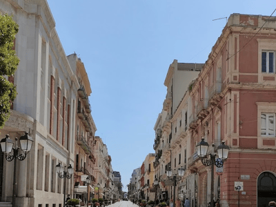 Lively street of Via d'Aquino, lined with historic buildings and lampposts, under a sunny sky.