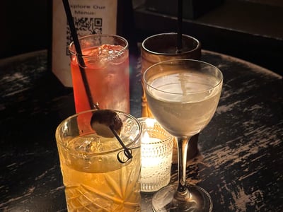 Four refined cocktails on a wooden table, illuminated by the light of a candle at Bathtub Gin.