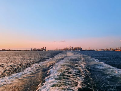 View from the Staten Island Ferry, showing the New York skyline at sunset and the waves behind the boat.