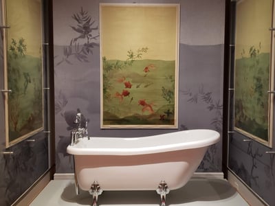 Vintage bathtub placed in a gallery of the Cooper Hewitt museum, surrounded by decorative murals.