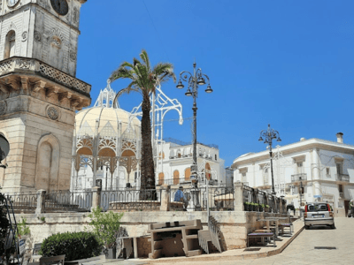 Picturesque place of Ceglie Messapica, with an old clock, palm trees, and sun-bleached buildings.