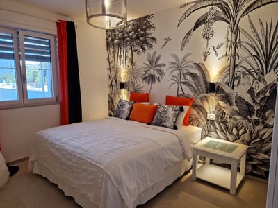 Chambre élégante à Résidence Papillon, décor tropical avec lit double et coussins colorés, idéale pour un séjour relaxant.