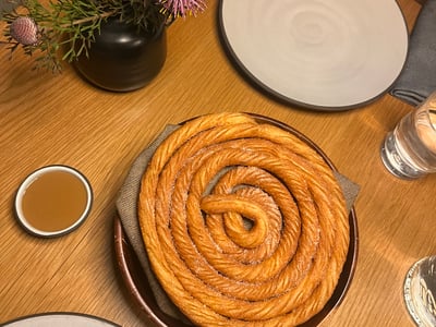 Golden spiral pastry presented on an elegant table at Cosme, accompanied by sauce in low light.