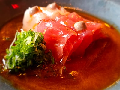 Fresh sashimi on a bed of sauce, garnished with green vegetables, showcasing the refined cuisine of Catch, in Paris.