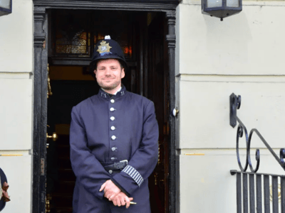 A Victorian police officer in uniform standing at the entrance of 221 B Baker Street, famous for its connection to Sherlock Holmes.