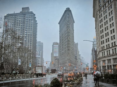 The Flatiron Building stands majestically under the snow, surrounded by the lively frenzy of the Flatiron district in New York.