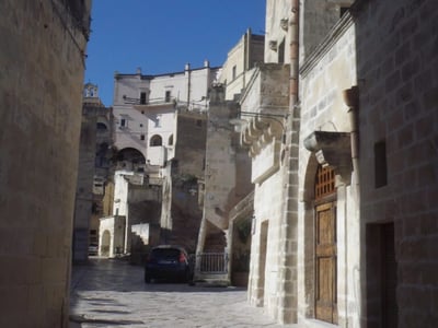 Rue pittoresque dans le Sasso Barisano, avec des bâtiments historiques et un ciel bleu clair. Atmosphère charmante et médiévale.