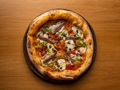 Pizza savoureuse de Pizzeria Uémé, garnie de tomates, mozzarella, anchois et légumes frais sur une croûte dorée.