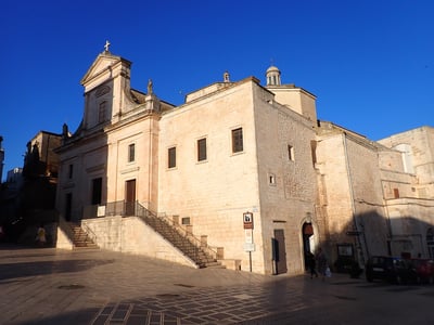 Église mère de San Nicola, caractérisée par son architecture en pierre claire et son ciel bleu, située à [lieu mieux connu].