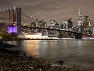 Night view of the illuminated Brooklyn Bridge, with the skyscrapers of Manhattan in the background. Dynamic urban atmosphere.