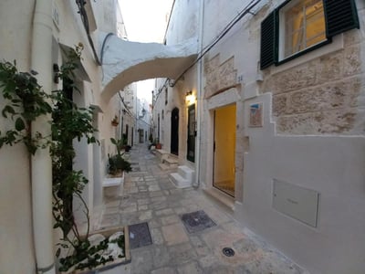 A picturesque alley in Cà under the arch, lined with white walls, plants, and colorful doors. Charming and welcoming atmosphere.