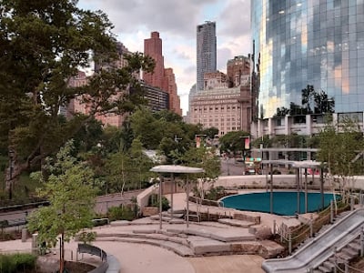 Parc Battery Playscape avec des structures de jeu modernes entourées de greenery et de bâtiments réfléchissants.